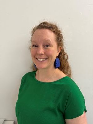 Magdalena hymyilee kameralle profiilikuvassa. Hänellä on kiharat punertavat hiukset, pisamia, siniset korvakorut ja kirkkaanvihreä paita.